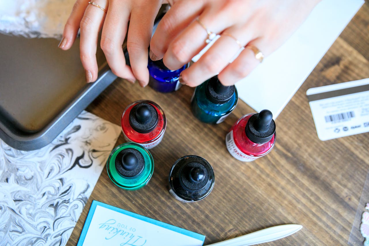 about-01 Hands arranging colorful ink bottles on a wooden desk in a creative workspace.