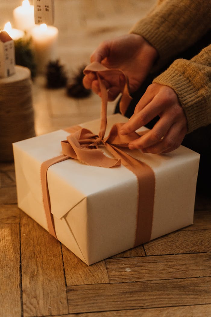 gallery-1 Hands carefully unwrap a gift box with a ribbon in a warm, cozy indoor setting.