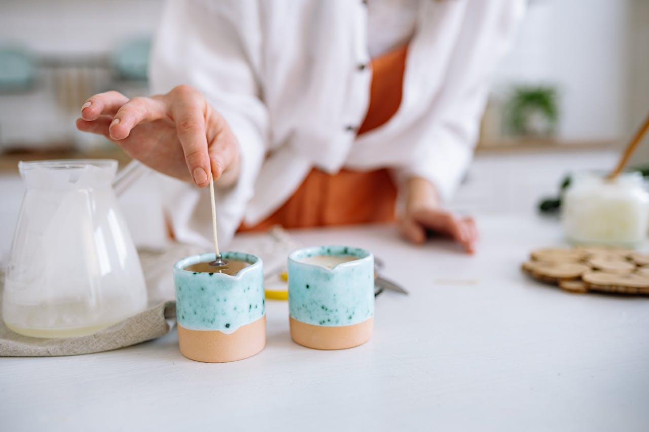 services-01 Close-up of hands making handmade candles using soy wax in decorative containers.